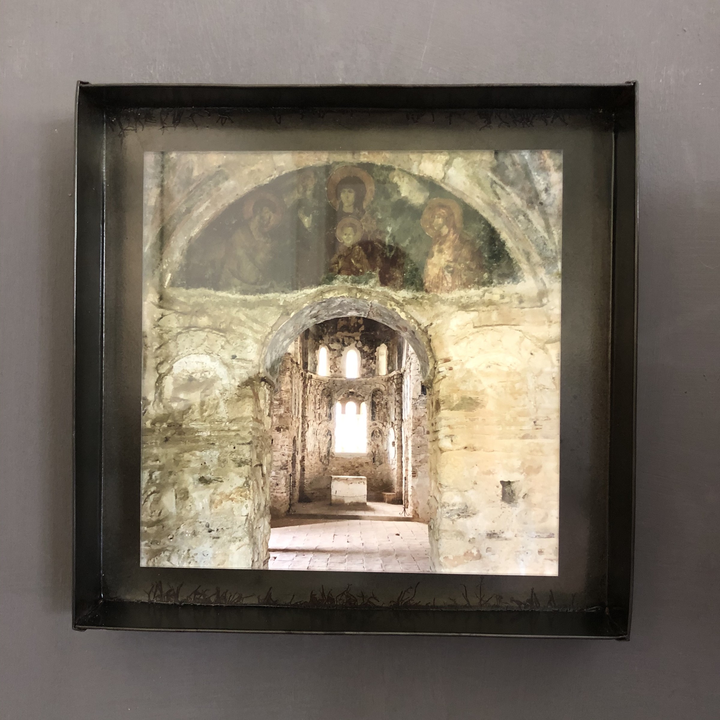 Een ingelijst beeld van een verweerd kerkinterieur met een hoge deuropening.